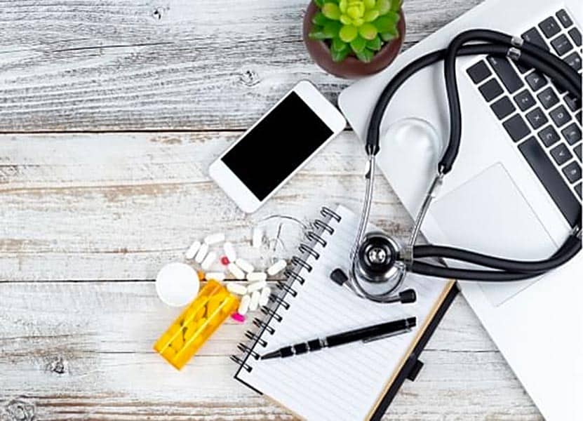 A stethoscope, laptop, plant, phone, bottle of pills, paper, and pen.