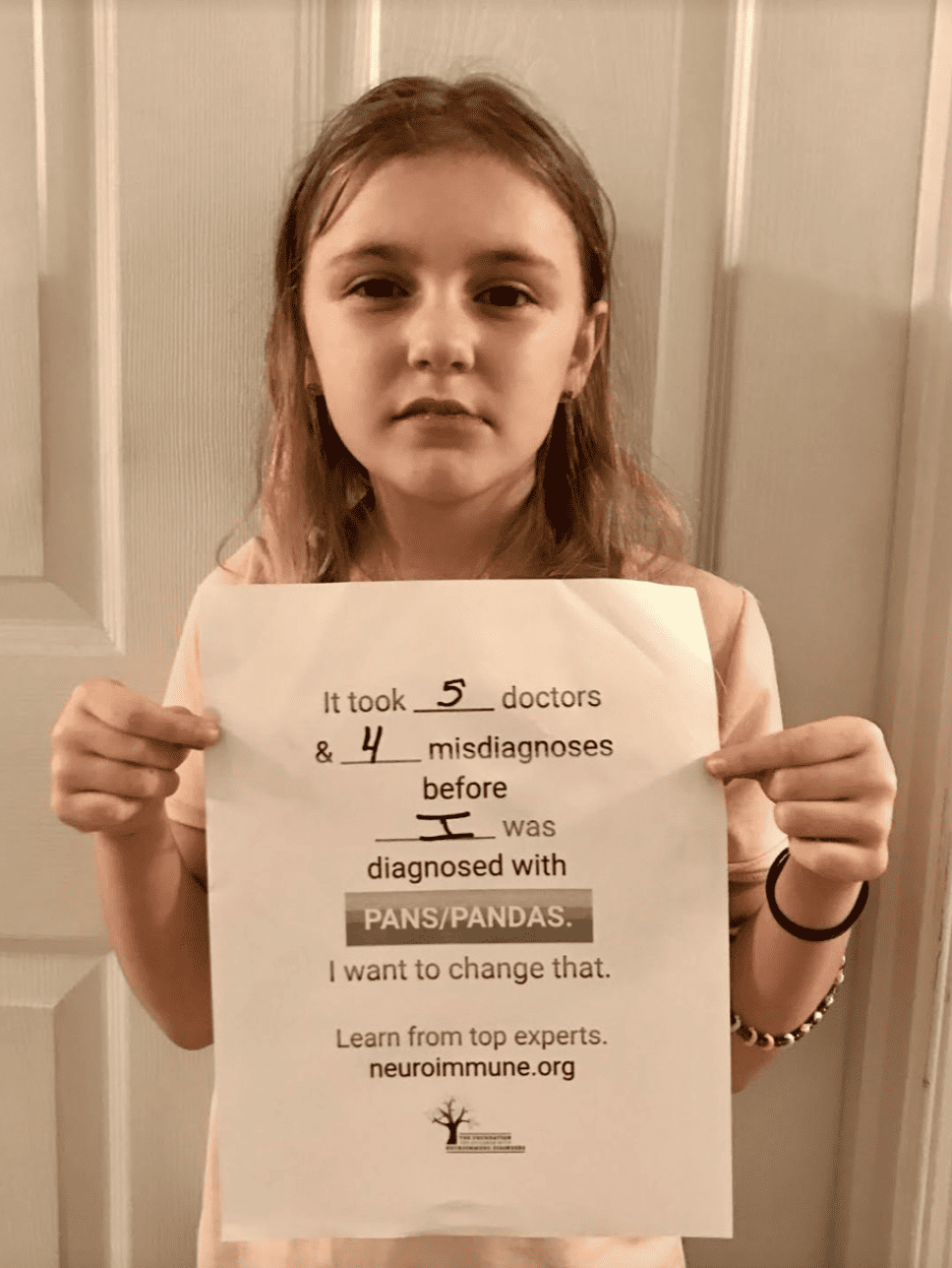 A young girl holding a paper that reads: It took 5 doctors & 4 misdiagnoses before I was diagnosed with PANS/PANDAS. I want to change that. Learn from top experts. neuroimmune.org.