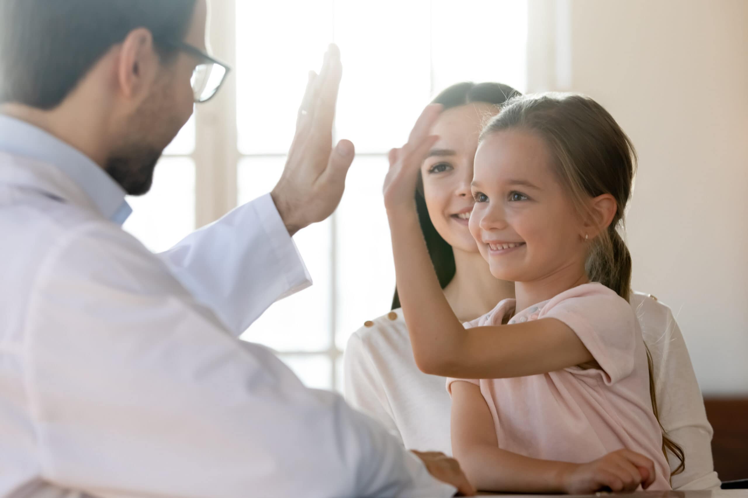 Young girl in a pink top giving a high five to her doctor wearing glasses.