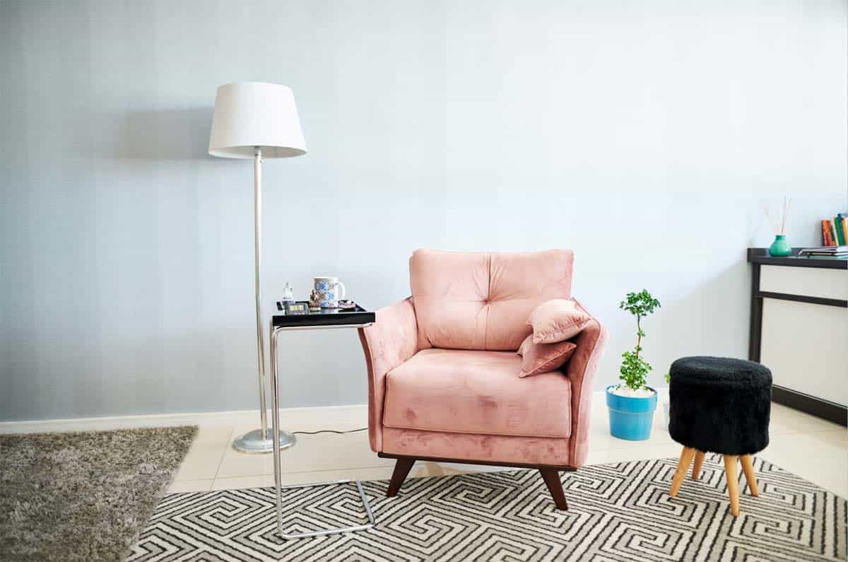 An upholstered pink chair with a black stool, a floor lamp, and a side table with a mug in a therapist's office.